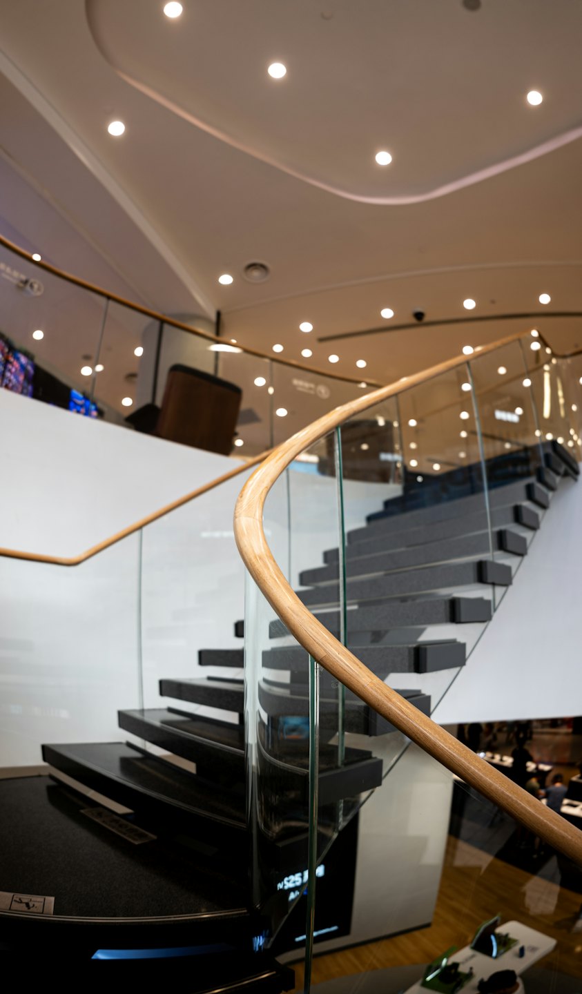 Moderne geschwungene Treppe mit Glasgeländer führt durch ein Gebäude.