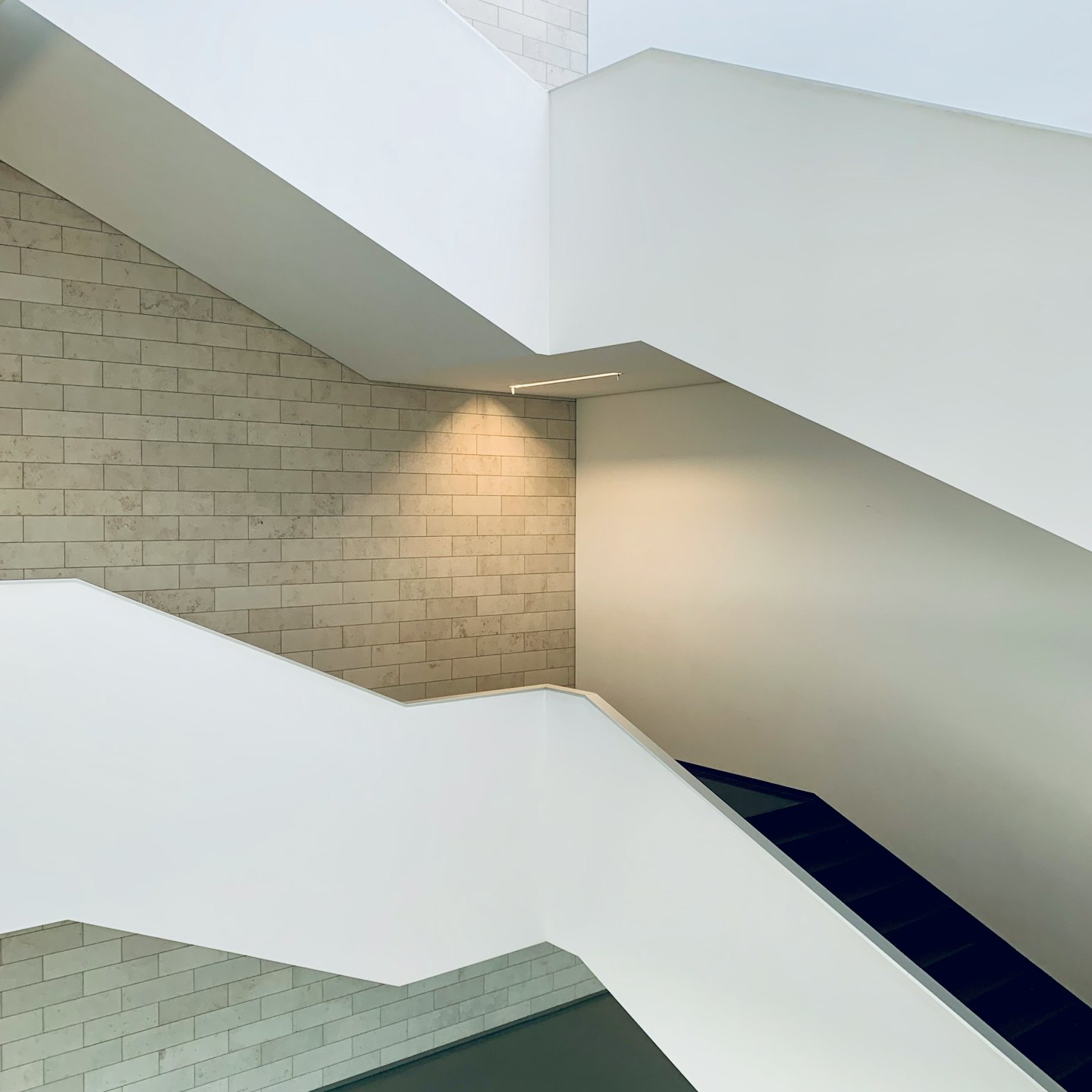 Moderne mehrstufige Treppe mit weißen Geländern und Ziegelwand.